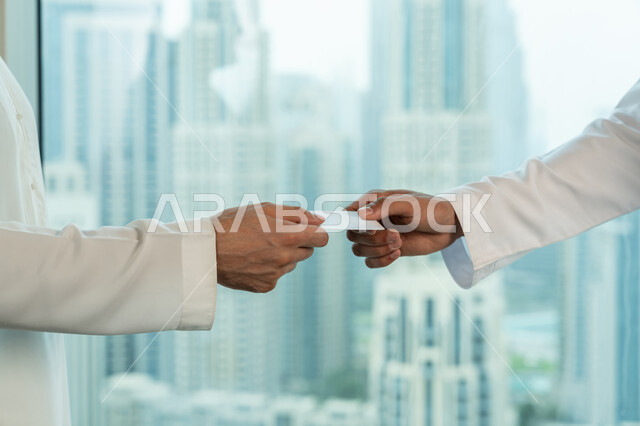 صداقات وبناء علاقات اجتماعية، موك أب أبيض مستطيل فارغ، صورة مقربة لايدي رجلي اعمال عربيين خليجيين اماراتيين يقومان بتبادل البطاقات التعريفية، الشراكة في الأعمال والمشاريع، مفهوم التعارف والتحاور