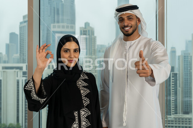 التفاهم والتعاون بين الزملاء لتحقيق أهداف الشركة، تعابير الجودة والامتياز، صورة مقربة لموظفين عربيين خليجيان اماراتيين يقفان باستقمامة يرفعان يديهما بايماءات القبول والموافقة، بيئة العمل المريحة في شركات الامارات