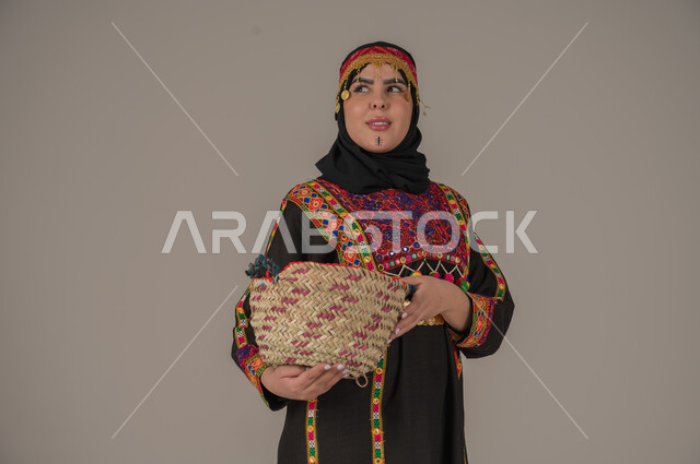 مهن وحرف يدوية شعبية, الفخر بالتراث التاريخي، بورتريه مقرب لإمرأة عربية خليجية سعودية ترتدي الكرتة والهامة تحمل سلة مصنوعة من القش, ارتداء زي المنطقة الوسطى في المناسبات الوطنية، يوم بدينا 1727م, ذكرى تأسيس الدولة السعودية الأولى في 22 فبراير, خلفية رمادية