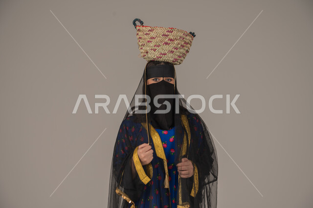 ذكرى تأسيس الدولة السعودية الأولى 22 فبراير, الفخر بالتراث التاريخي، مهن يدوية شعبية, ارتداء زي المنطقة الوسطى في المناسبات الوطنية، يوم بدينا 1727م، بورتريه مقرب لإمرأة عربية خليجية سعودية ترتدي البرقع والشيلة تضع سلة قش على رأسها، خلفية رمادية