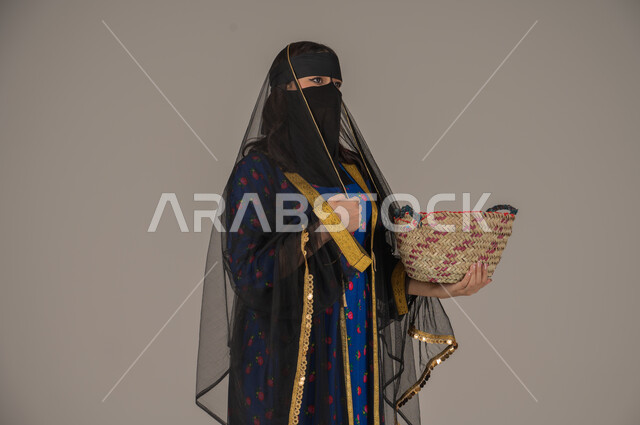 حرف ومهن يدوية شعبية, ارتداء زي المنطقة الوسطى في المناسبات الوطنية، يوم بدينا 1727م، ذكرى تأسيس الدولة السعودية الأولى 22 فبراير, الفخر بالتراث التاريخي، بورتريه لإمرأة عربية خليجية سعودية ترتدي البرقع والشيلة تحمل سلة مصنوعة من القش, خلفية رمادية