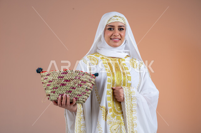 مهن وحرف يدوية شعبية قديمة، بورتريه لامرأة عربية خليجية سعودية مبتسمة ترتدي الشيلة والنشل تمسك بيدها سلة مصنوعة من القش، النظر إلى الكاميرا بتعابير الفخر والاعتزاز، يوم بدينا١٧٢٧م، ارتداء أزياء المنطقة الشرقية، ذكرى تأسيس الدولة السعودية الأولى٢٢فبراير، خلفية بنية