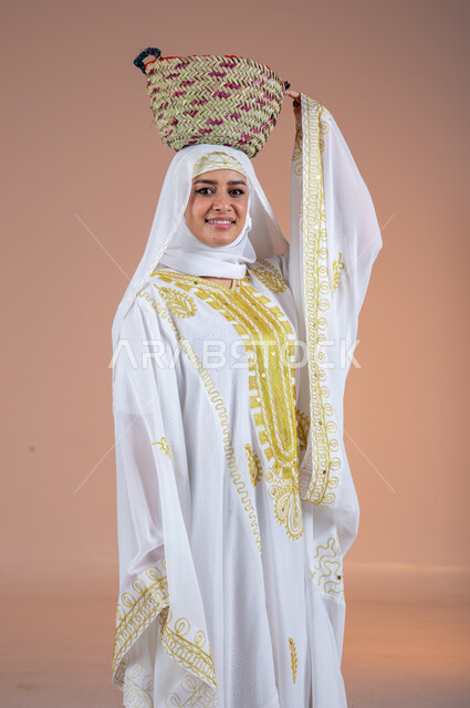 النظر الى الكاميرا بتعابير الفخر والاعتزاز،مهن وحرف يدوية شعبية قديمة، ارتداء أزياء المنطقة الشرقية، يوم بدينا1727م، بورتريه لإمرأة عربية خليجية سعودية مبتسمة ترتدي الشيلة والنشل تضع على رأسها سلة قش، ذكرى تأسيس الدولة السعودية الأولى في 22 فبراير، خلفية ملونة