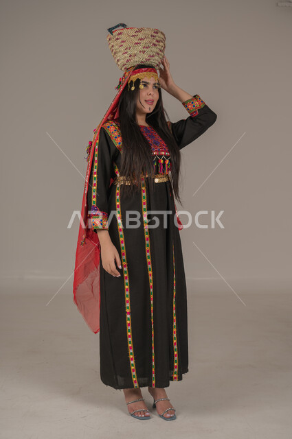 مهن وحرف يدوية شعبية، يوم بدينا ١٧٢٧م، بورتريه لإمرأه عربيه سعوديه خليجيه ترتدي الهامة والكرتة تضع على رأسها سلة قش، النظر الى مكان ما بتعابير الفخر والاعتزاز، ذكرى تأسيس الدولة السعودية الأولى٢٢ فبراير, ارتداء أزياء المنطقة الوسطى, الجسم الكامل بالطول، خلفيه رمادية