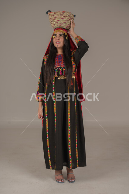 مهن وحرف يدوية شعبية، يوم بدينا ١٧٢٧م، بورتريه لإمرأه عربيه سعوديه خليجيه ترتدي الهامة والكرتة تضع على رأسها سلة قش، النظر الى مكان ما بتعابير الفخر والاعتزاز، ذكرى تأسيس الدولة السعودية الأولى٢٢ فبراير, ارتداء أزياء المنطقة الوسطى, الجسم الكامل بالطول، خلفيه رمادية