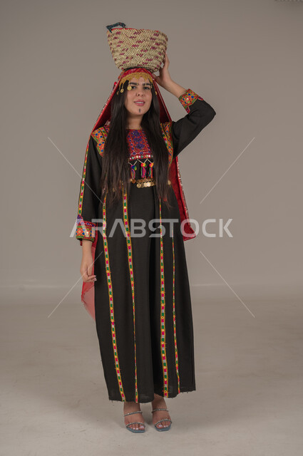 النظر الى الكاميرا بتعابير الفخر والاعتزاز، مهن وحرف يدوية شعبية، يوم بدينا ١٧٢٧م، بورتريه لإمرأه عربيه سعوديه خليجيه ترتدي الهامة والكرتة تضع على رأسها سلة قش، ذكرى تأسيس الدولة السعودية الأولى٢٢ فبراير, ارتداء أزياء المنطقة الوسطى, الجسم الكامل بالطول، خلفيه رمادية