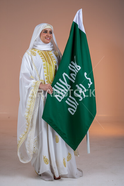 يوم العلم السعودي11 مارس، يوم بدينا 1727 م، ارتداء أزياء المنطقة الشرقية، بورتريه لإمرأة عربية خليجية سعودية مبتسمة ترتدي الشيلة والنشل تحمل بيدها علم يوم التأسيس، ذكرى تأسيس الدولة السعودية الأولى، الاحتفال بالمناسبات والأعياد الوطنية الشعبية، خلفية بنية