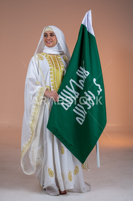 يوم العلم السعودي11 مارس، يوم بدينا 1727 م، ارتداء أزياء المنطقة الشرقية، بورتريه لإمرأة عربية خليجية سعودية مبتسمة ترتدي الشيلة والنشل تحمل بيدها علم يوم التأسيس، ذكرى تأسيس الدولة السعودية الأولى، الاحتفال بالمناسبات والأعياد الوطنية الشعبية، خلفية بنية