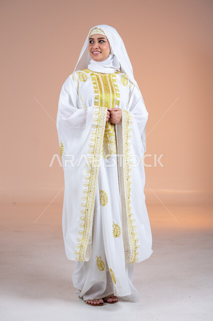 الاهتمام بالمظهر الخارجي والنعومة، بورتريه لامرأة عربية خليجية سعودية مبتسمة ترتدي الشيلة والنشل تنظر الى مكان ما بتعابير الفخر والاعتزاز، يوم بدينا١٧٢٧م، ارتداء أزياء المنطقة الشرقية، ذكرى تأسيس الدولة السعودية الأولى٢٢فبراير، الجسم الكامل بالطول، خلفية بنية