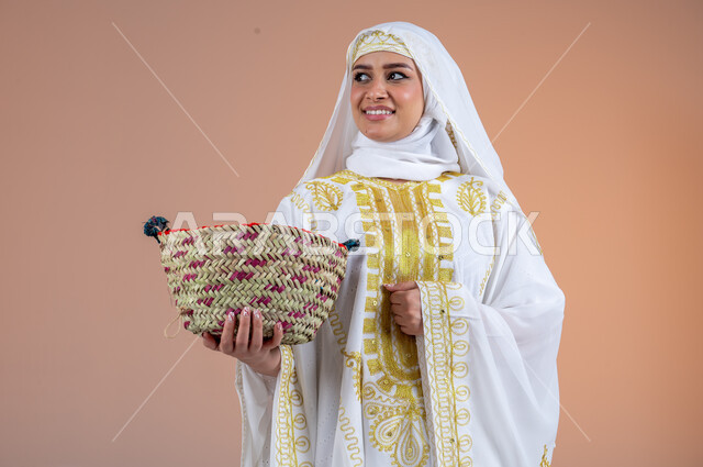 النظر إلى مكان ما بتعابير الفخر والاعتزاز، يوم بدينا١٧٢٧م، مهن وحرف يدوية شعبية قديمة، بورتريه لامرأة عربية خليجية سعودية مبتسمة ترتدي الشيلة والنشل تمسك بيدها سلة قش، ارتداء أزياء المنطقة الشرقية، ذكرى تأسيس الدولة السعودية الأولى٢٢فبراير، خلفية بنية
