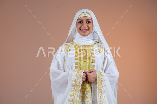 مفهوم الانوثة والاهتمام بالمظهر الخارجي، بورتريه لامرأة عربية خليجية سعودية مبتسمة ترتدي الشيلة والنشل تنظر الى الكاميرا بتعابير الفخر والاعتزاز، يوم بدينا١٧٢٧م، ارتداء أزياء المنطقة الشرقية في المناسبات الوطنية، ذكرى تأسيس الدولة السعودية الأولى٢٢فبراير، خلفية بنية