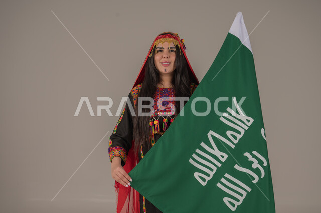الاحتفال بالمناسبات الوطنية الشعبية, يوم بدينا ١٧٢٧م، بورتريه لإمرأه عربيه سعوديه خليجيه ترتدي الهامة والكرتة تحمل بيدها علم يوم التأسيس، يوم العلم السعودي١١ مارس,  ذكرى تأسيس الدولة السعودية الأولى، ارتداء ازياء المنطقة الوسطى, تعابير الفخر والاعتزاز، خلفيه رمادية