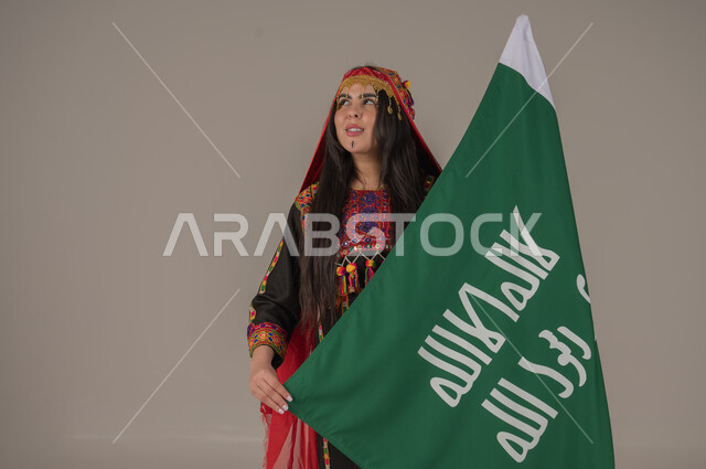 الاحتفال بالمناسبات الوطنية الشعبية, يوم بدينا ١٧٢٧م، بورتريه لإمرأه عربيه سعوديه خليجيه ترتدي الهامة والكرتة تحمل بيدها علم يوم التأسيس، يوم العلم السعودي١١ مارس,  ذكرى تأسيس الدولة السعودية الأولى، ارتداء ازياء المنطقة الوسطى, تعابير الفخر والاعتزاز، خلفيه رمادية