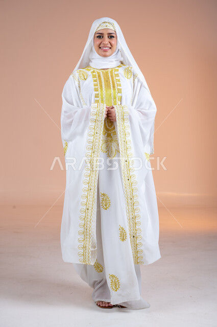الانوثة والاهتمام بالمظهر الخارجي، بورتريه لامرأة عربية خليجية سعودية مبتسمة ترتدي الشيلة والنشل تنظر الى الكاميرا بتعابير الفخر والاعتزاز، يوم بدينا١٧٢٧م، ارتداء أزياء المنطقة الشرقية، ذكرى تأسيس الدولة السعودية الأولى٢٢فبراير، الجسم الكامل بالطول، خلفية ملونة
