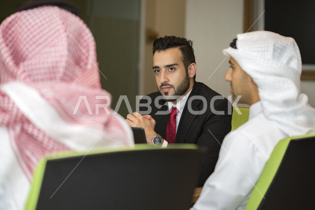 اجتماع اداري بمجموعة من الأشخاص السعوديين الخليجيين مع رجل عربي ببدلة يتناقشون في غرفة الاجتماعات، شركة سعودية، شركاء العمل ، بيئة العمل، وظائف ومهن مكتبية، إجتماع عمل في مقر شركة، توقيع العقود