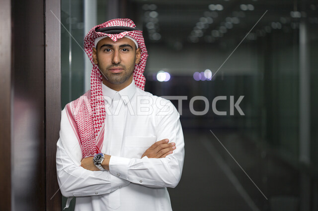 صورة مقربة لرجل أعمال عربي سعودي خليجي مع خلفية المكتب  ، يرتدي الزي السعودي التقليدي ، بأيدي متقاطعه في مقرعمله بالشركة ، شركة سعودية ، وظائف ومهن مكتبية ، بيئة العمل 
