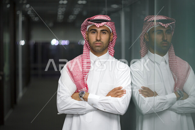 صورة مقربة لرجل أعمال عربي سعودي خليجي مع خلفية المكتب  ، يرتدي الزي السعودي التقليدي ، بأيدي متقاطعه في مقرعمله بالشركة ، شركة سعودية ، وظائف ومهن مكتبية ، بيئة العمل 