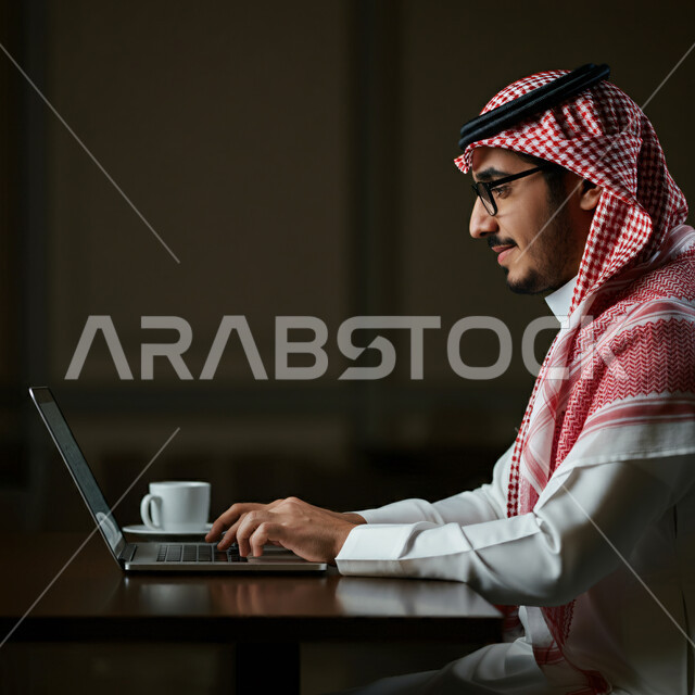 إدارة مهام العمل اليومية في مقر الشركة، مهن ووظائف سعودية، استخدام الأجهزة التقنية الحديثة، رجل عربي خليجي سعودي يرتدي الثوب التقليدي والشماغ يجلس في مكتبه يعمل على جهاز الحاسوب المحمول، تطوير الخطط والاسترتيجيات