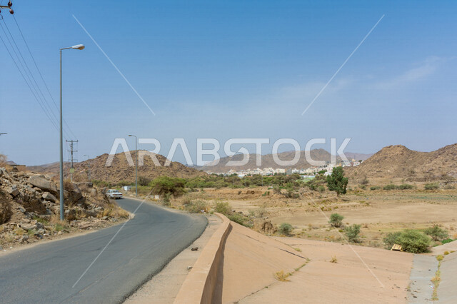 صورة مقربة لطريق صحراوي، الرمال الصحراوية، الطبيعة الجبلية، الاشجار والمباني، سيارة وعمدان اضاءة 