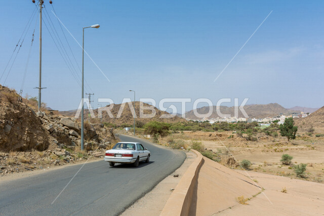 صورة مقربة لطريق صحراوي، الرمال الصحراوية، الطبيعة الجبلية، الاشجار والمباني، سيارة وعمدان اضاءة 