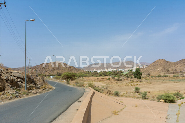 صورة مقربة لطريق صحراوي، الرمال الصحراوية، الطبيعة الجبلية، الاشجار والمباني، سيارة وعمدان اضاءة 