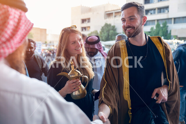 استقبال السياح الاجانب في الرياض في المملكة العربية السعودية، تقاليد وعادات شعبية في حسن الضيافة، تصوير مقرب لسواح اجانب يرتدون البشت السعودي المطرز، فتح ابواب السياحه السعودية، أماكن ومعالم سياحيه