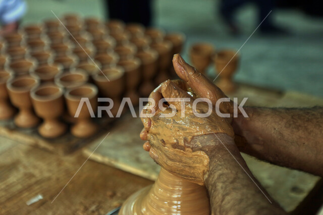 ممارسة مهارة صنع الفخار،  محترف عربي سعودي خليجي يعمل في ورشة الاعمال الفنية،  احتراف تصنيع الخزف والفخاريات، أعمال يدوية سعودية، صوره مقربة لايدي حرفي يقوم بصنع الفخار