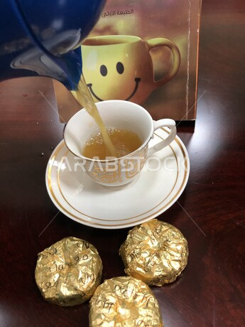 صورة مقربة لفنجان القهوة العربية ومعمول بالتمر على طاولة خشبية ، اعداد القهوه العربية ،  صب القهوة ، مشروب ساخن ، القهوه العربية