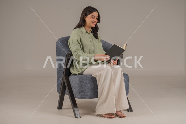 قراءة الروايات والقصص، ايماءات التركيز والاستمتاع، تمضية أوقات الفراغ بالتعلم والتثقيف الذاتي، بورتريه لامراة عربية سعودية خليجية ترتدي ثياب كاجوال تحمل بيدها كتاب, خلفية بيج 