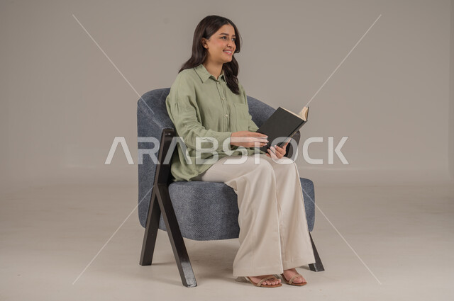 قراءة الروايات والقصص، ايماءات التركيز والاستمتاع، تمضية أوقات الفراغ بالتعلم والتثقيف الذاتي، بورتريه لامراة عربية سعودية خليجية ترتدي ثياب كاجوال تحمل بيدها كتاب, خلفية بيج 