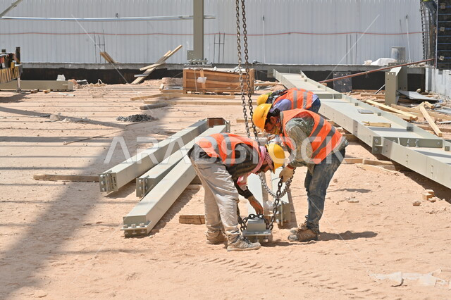 Implementing the construction plan and forming the metal structure, heavy equipment, cranes and high scaffolding used in the project site, construction works, pouring concrete and laying the initial foundations, Saudi Arabian Gulf workers wearing protective jackets and helmets working in a building under construction and erection
