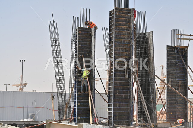 تنفيذ مخطط الإعمار وتشكيل الهيكل المعدني، المعدات الثقيلة والرافعات والسقالات العالية المستخدمة في موقع المشروع، أعمال البناء وصب الخرسانات ووضع الأساسات الأولية، عمال عربيون خليجيون سعوديون يرتدون سترة وخوذة الحماية يقومون بالعمل في مبنى قيد الإنشاء والتشييد