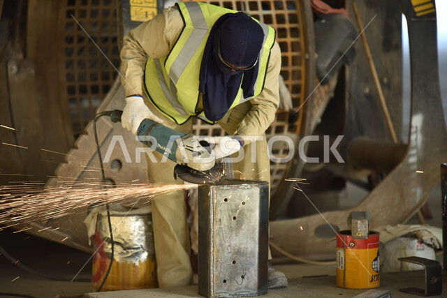 متابعة سير العمل في ورش الحدادة بمهارة وإتقان، ارتداء الزي الواقي للحماية من الشرار المتناثر في المعمل, عامل عربي خليجي سعودي يرتدي قناع الحماية والقفازات يقوم بلحام المعدن وصهره, تجهيز وتوصيل الحديد بمعدات وأدوات لحامية خاصة، وظائف ومهن صناعية للشباب السعودي