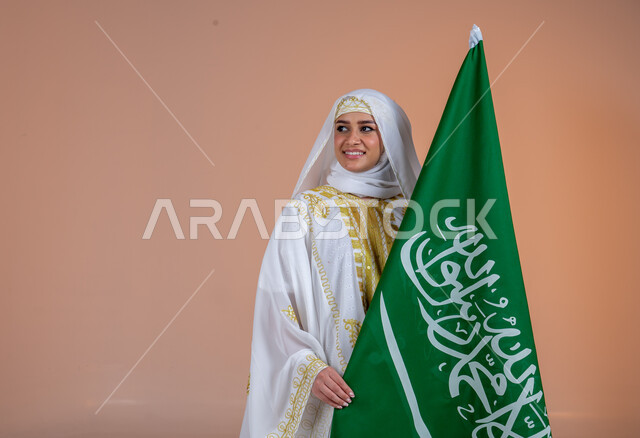 ارتداء أزياء المنطقة الشرقية في المناسبات والأعياد الوطنية، بورتريه مقرب لإمرأة عربية خليجية سعودية مبتسمة ترتدي الشيلة والنشل تحمل بيدها علم المملكة، يوم بدينا 1727 م، ذكرى تأسيس الدولة السعودية الأولى 22 فبراير، خلفية ورية