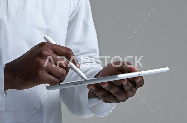 التقنيات الحديثة المتطورة، بورتريه مقرب ليد رجل عربي خليجي سعودي يرتدي الثوب التقليدي يحمل جهاز آيباد ويستخدم قلم ستايلس للكتابة أو الرسم على الشاشة، التسويق لموقع إلكتروني، استخدام قلم التابليت لتدوين الملاحظات، برامج التواصل الاجتماعي، خلفية بيضاء