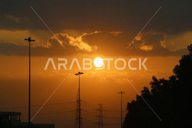 صورة توضيحية للمباني وأعمدة الكهرباء اثناء غروب الشمس، منظر طبيعي خلاب اثناء الغروب، جمال المباني والاشجار مع غروب الشمس