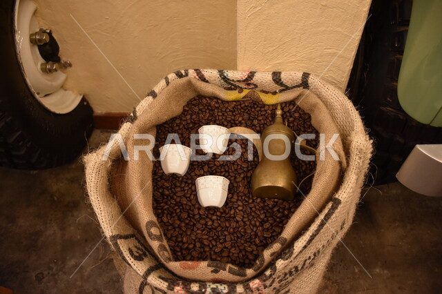 صورة لإبريق عربي قديم من النحاس مع فناجين داخل كيس من البن، الضيافة عند العرب، ديكور عربي، دلة القهوة العربية