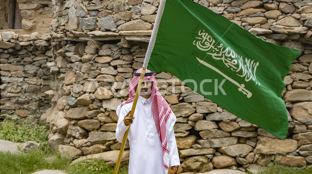 رجل عربي خليجي سعودي يرتدي الزي التقليدي السعودي ، بيده علم المملكة العربية السعودية ،ذكرى اليوم الوطني السعودي ، الاحتفال بالعيد الوطني السعودي
