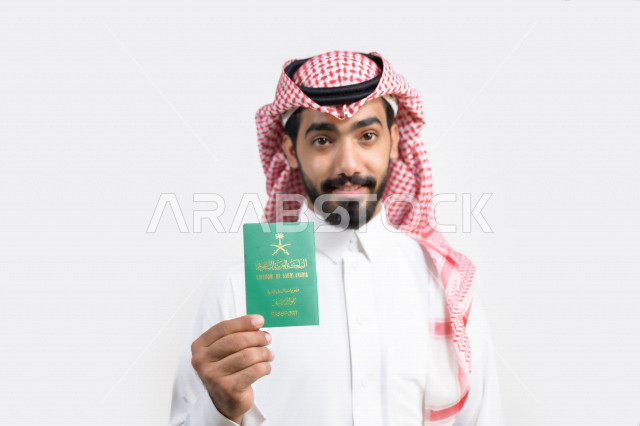 Portrait of a Saudi Arabian Gulf Arab man holding the Saudi passport with gestures of happiness, official document, international travel of Saudi citizens, Saudi National Day, National Day celebration, white background