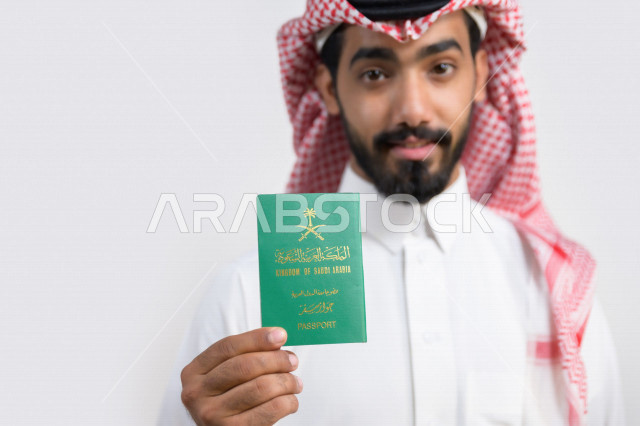 بورتريه لرجل عربي خليجي سعودي يحمل بيده جواز السفر السعودي بإيماءات تدل على السعادة ، وثيقة رسمية ، سفر المواطنين السعوديين دوليا ، اليوم الوطني السعودي ، الإحتفال بالعيد الوطني ، خلفية بيضاء