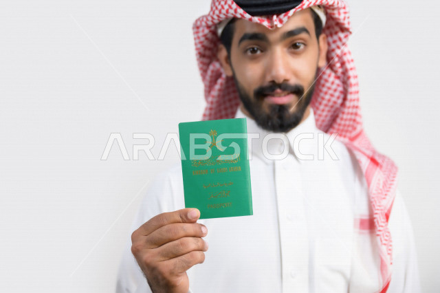 بورتريه لرجل عربي خليجي سعودي يحمل بيده جواز السفر السعودي بإيماءات تدل على السعادة ، وثيقة رسمية ، سفر المواطنين السعوديين دوليا ، اليوم الوطني السعودي ، الإحتفال بالعيد الوطني ، خلفية بيضاء
