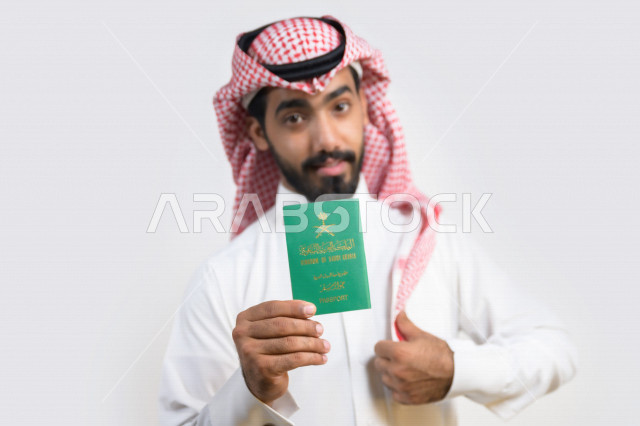 Portrait of a Saudi Arabian Gulf Arab man holding the Saudi passport with gestures of happiness, official document, international travel of Saudi citizens, Saudi National Day, National Day celebration, white background