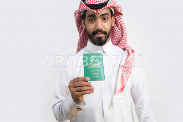بورتريه لرجل عربي خليجي سعودي يحمل بيده جواز السفر السعودي بإيماءات تدل على السعادة ، وثيقة رسمية ، سفر المواطنين السعوديين دوليا ، اليوم الوطني السعودي ، الإحتفال بالعيد الوطني ، خلفية بيضاء