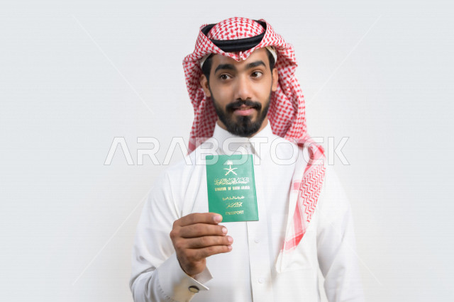 Portrait of a Saudi Arabian Gulf Arab man holding the Saudi passport with gestures of happiness, official document, international travel of Saudi citizens, Saudi National Day, National Day celebration, white background