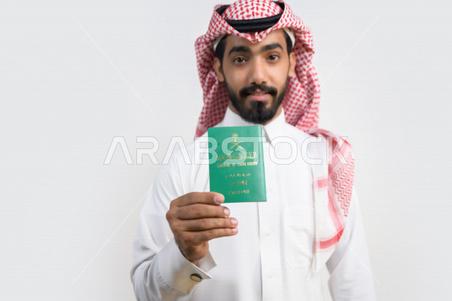 بورتريه لرجل عربي خليجي سعودي يحمل بيده جواز السفر السعودي بإيماءات تدل على السعادة ، وثيقة رسمية ، سفر المواطنين السعوديين دوليا ، اليوم الوطني السعودي ، الإحتفال بالعيد الوطني ، خلفية بيضاء