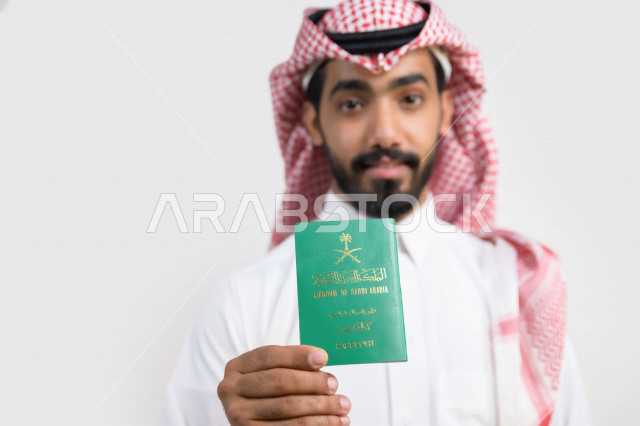 Portrait of a Saudi Arabian Gulf Arab man holding the Saudi passport with gestures of happiness, official document, international travel of Saudi citizens, Saudi National Day, National Day celebration, white background