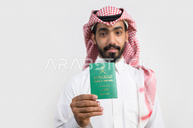 Portrait of a Saudi Arabian Gulf Arab man holding the Saudi passport with gestures of happiness, official document, international travel of Saudi citizens, Saudi National Day, National Day celebration, white background