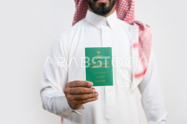 بورتريه لرجل عربي خليجي سعودي يحمل بيده جواز السفر السعودي ، وثيقة رسمية ، سفر المواطنين السعوديين دوليا ، اليوم الوطني السعودي ، الإحتفال بالعيد الوطني ، خلفية بيضاء