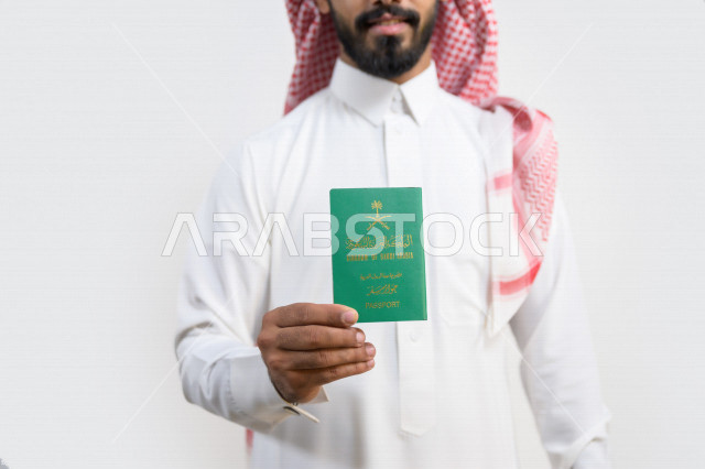 بورتريه لرجل عربي خليجي سعودي يحمل بيده جواز السفر السعودي ، وثيقة رسمية ، سفر المواطنين السعوديين دوليا ، اليوم الوطني السعودي ، الإحتفال بالعيد الوطني ، خلفية بيضاء