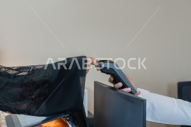 The possibility of paying bills using electronic cards, the development of technology and technology, a close-up image of the hand of an Arab Gulf Emirati woman wearing a black abaya paying at the cashier using a bank credit card, the use of modern means and technologies, facilitating the buying and selling processes